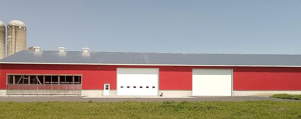 A large red barn with a metallic roof, 2 silos, and 2 large sectional garage doors